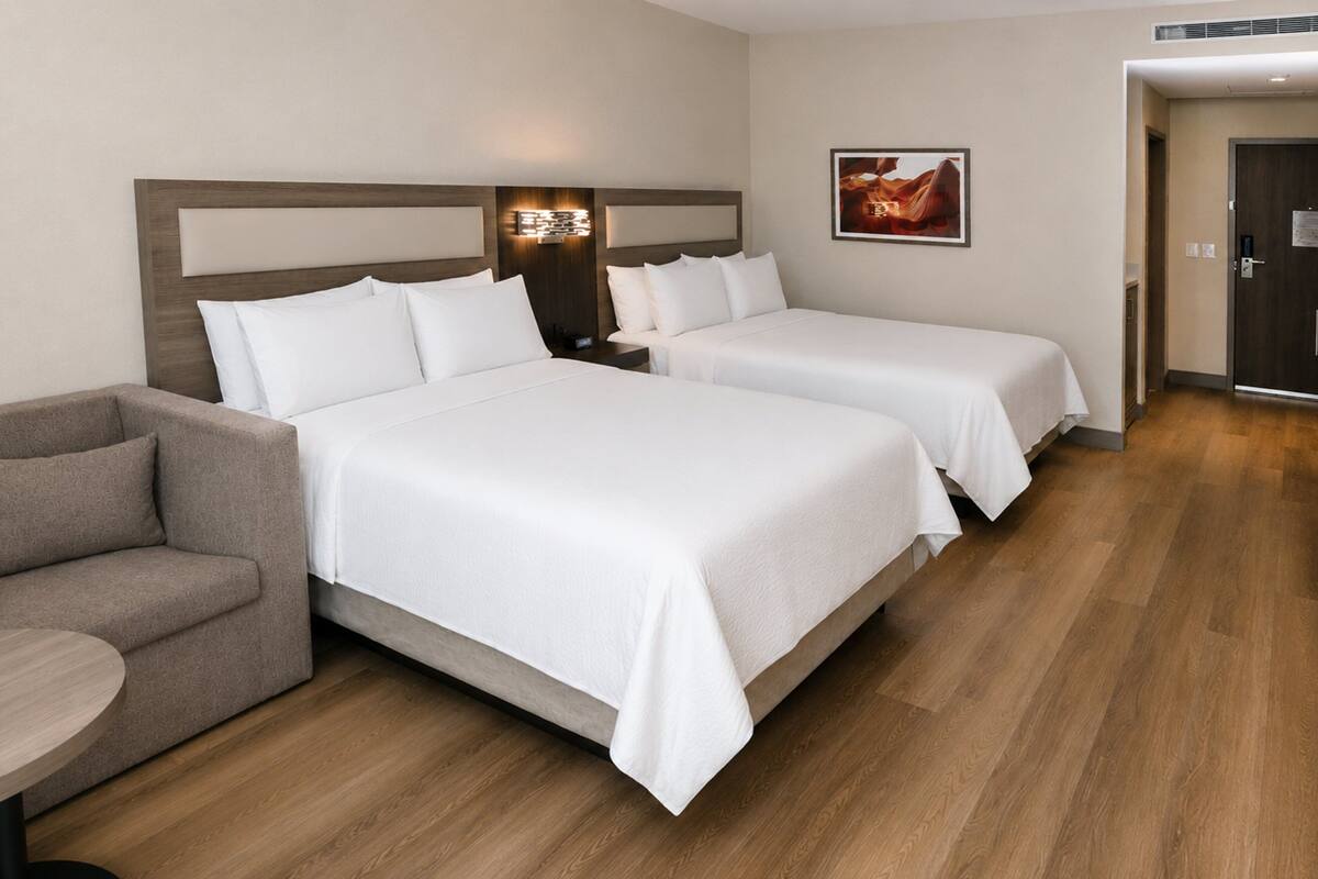 A hotel room with two beds, a sofa, a nightstand, and a wall-mounted lamp.