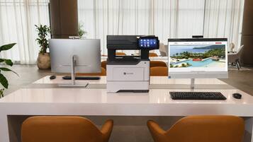 Una oficina moderna con una impresora Lexmark, una computadora de escritorio y un monitor que muestra una imagen de un resort tropical.