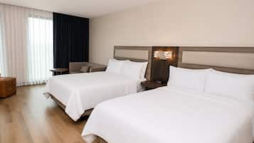 Camera d'albergo con due letti, un comodino, una lampada, una sedia e una finestra con tende.