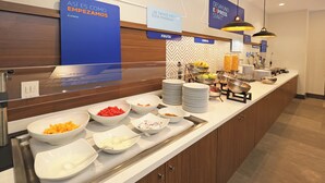 Mostrador de buffet con diversos alimentos y un cartel que indica opciones para desayuno.