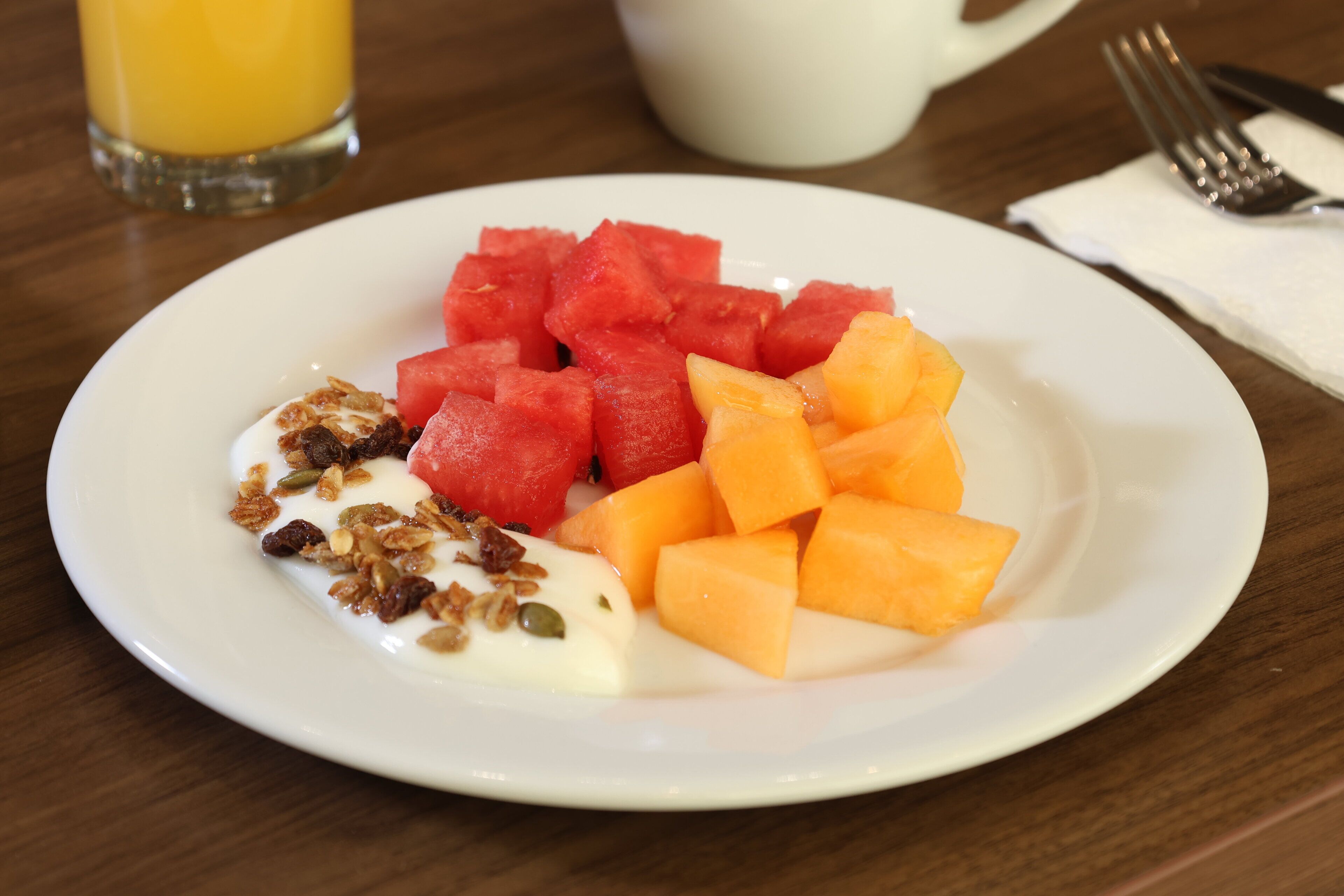 A plate of watermelon, cantaloupe, yogurt, and granola on a wooden table.