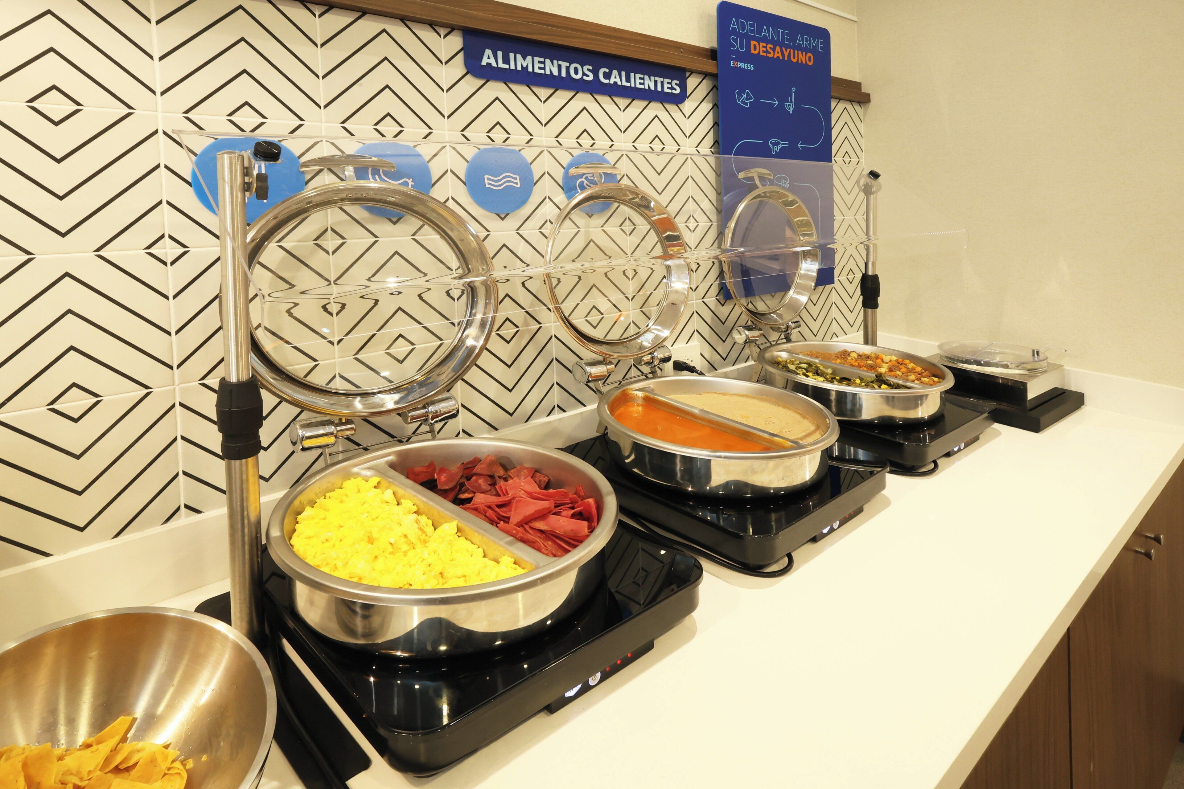 Ein Buffet mit verschiedenen Speisen, eine Wand mit geometrischem Muster und ein Schild, das auf heiße Speisen hinweist.