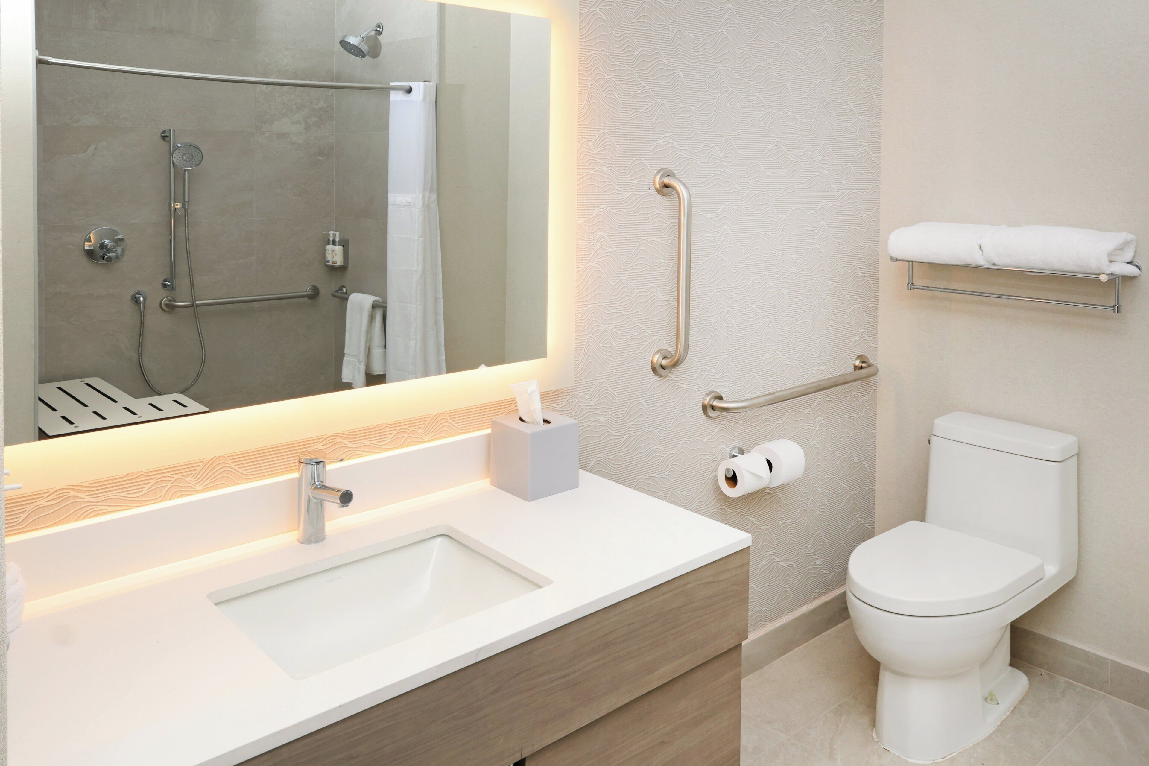 Ein modernes Badezimmer mit Waschbecken, Spiegel, Dusche, Toilette und Haltegriffen.