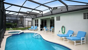Una piscina con cerramiento de vidrio, sillas reclinables azules y un jacuzzi.