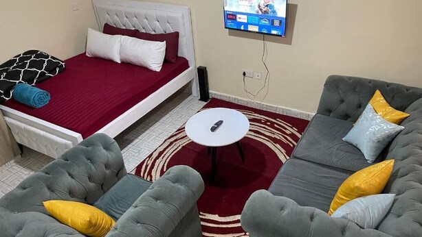 Una habitación con una cama, dos sofás, una mesita y un televisor montado en la pared.