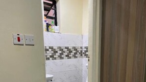 Un baño con inodoro, suelo de baldosas y un par de chanclas sobre un tapete.