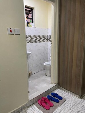 Ein Badezimmer mit Toilette, gefliestem Boden und einem Paar Flip-Flops auf einer Matte.