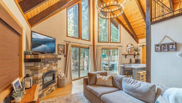 A cozy living room with a fireplace, large windows, and a comfortable sofa. - West Shore Tahoe Cabin - Loft Movie Nights, Pets (Tahoma)