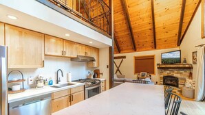 A spacious kitchen with wooden cabinets, a large island, and a dining area with chairs. - West Shore Tahoe Cabin - Loft Movie Nights, Pets (Tahoma)