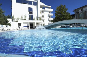 Una piscina dalle acque cristalline, circondata da edifici bianchi con balconi e un design architettonico moderno.
