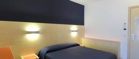 A hotel room with a bed, bedside tables, and a door.