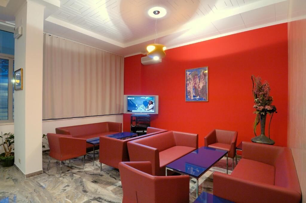 Una habitación de hotel con paredes rojas, una televisión, asientos rojos y un ventanal grande.