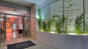 Een moderne hotellobby met een receptiebalie, een zithoek en een grote glazen wand met bamboepotten.