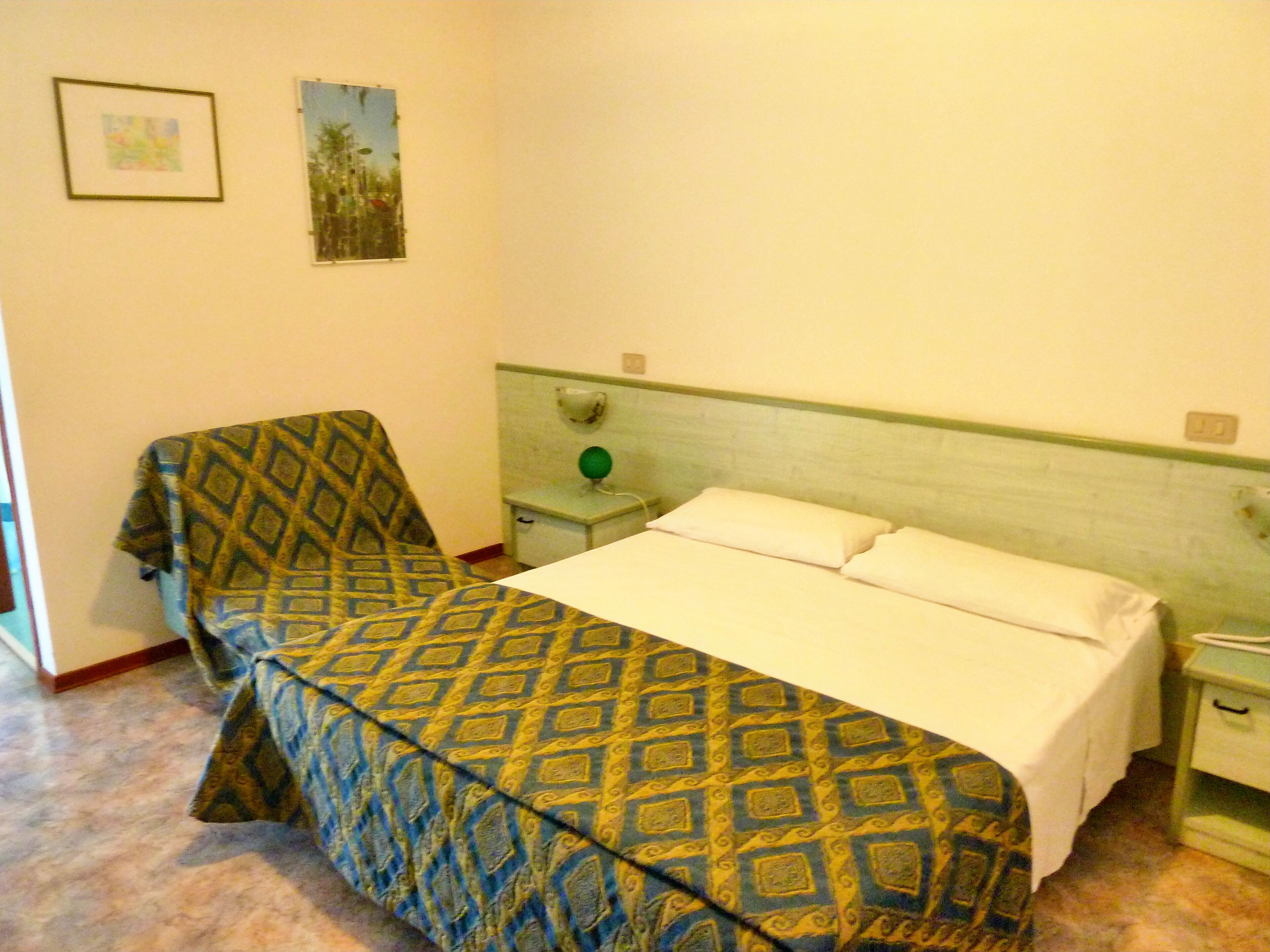 Ein Zimmer mit einem Bett, einem Sessel, einem Nachttisch und einer Wandlampe.