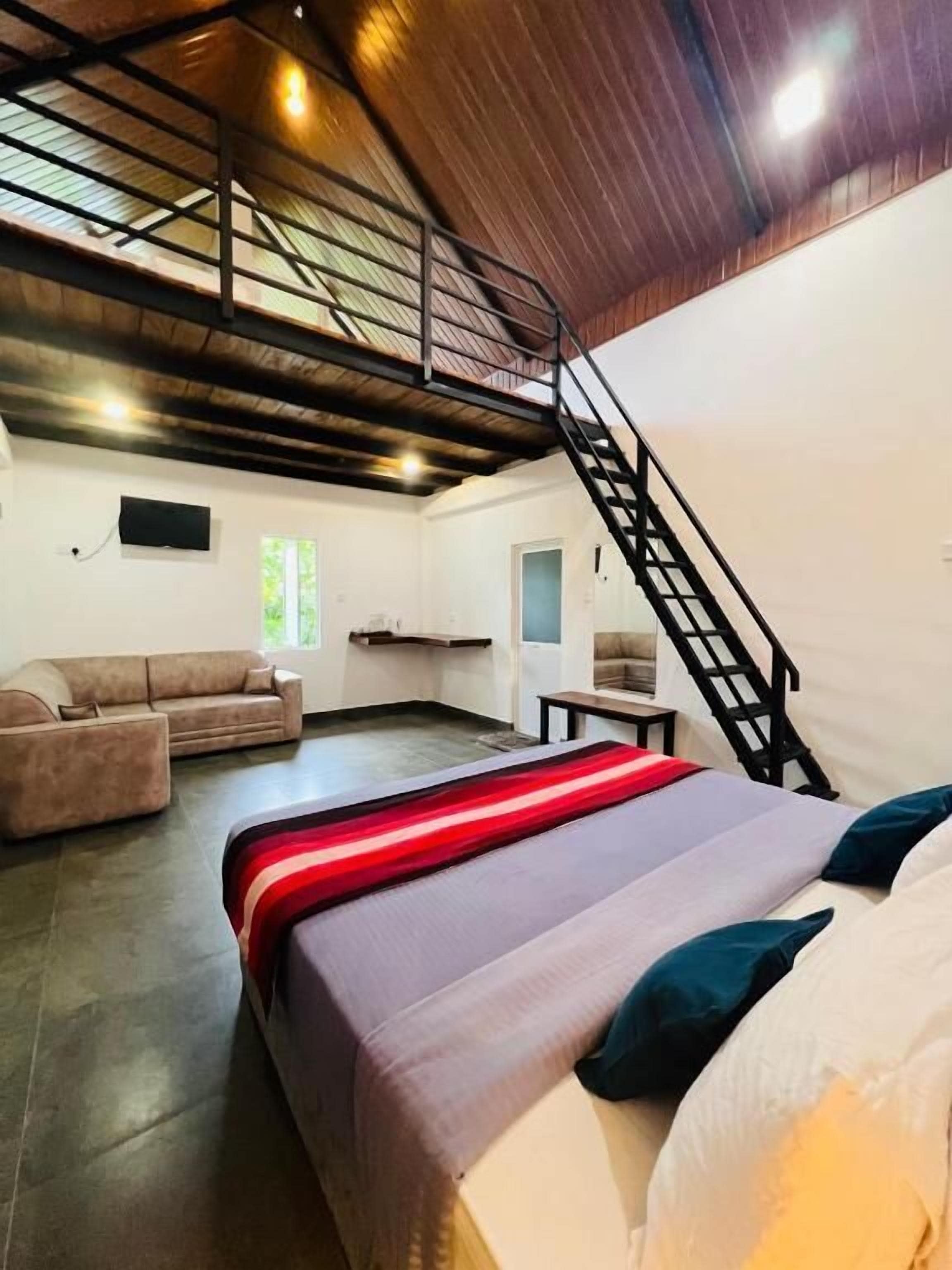 A spacious room with a bed, a sofa, a staircase, and a TV mounted on the wall.