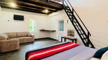 A spacious room with a bed, a sofa, a staircase, and a TV mounted on the wall.