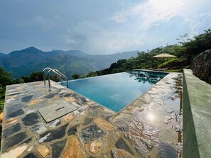 Una piscina infinita con suelo de piedra y vistas a montañas.