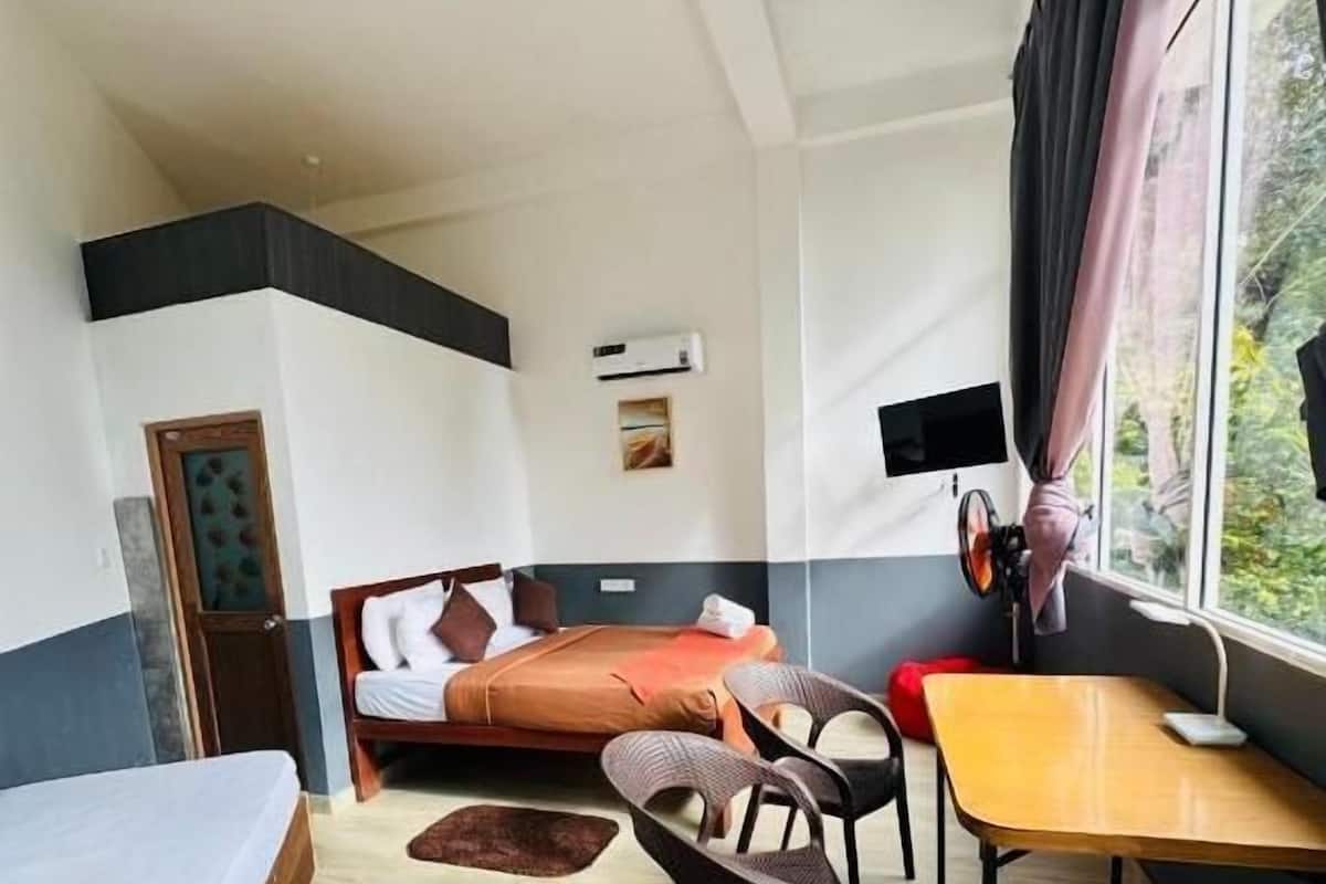 Una habitación de hotel con una cama, un escritorio, una silla, una ventana con cortinas, un equipo de aire acondicionado y un televisor montado en la pared.