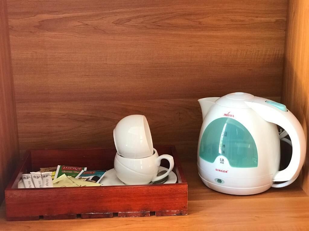 A wooden shelf with a white electric kettle and a tray containing a white mug and some books.