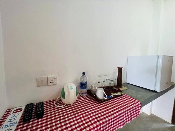 Una kitchenette pequeña con mantel a cuadros, una tetera, una botella de agua, vasos y una bandeja con una taza.