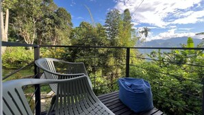 A balcony with two chairs and a blue bean bag, overlooking a lush garden and a mountain view.