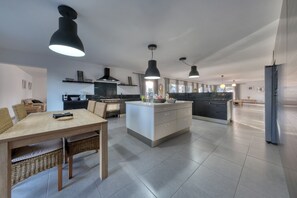 Une cuisine moderne dotée d’un îlot central, d’un éclairage suspendu et d’un coin repas avec des chaises en osier.