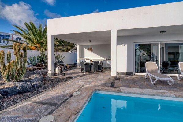 Un espace piscine extérieur moderne, doté d’une piscine à l’eau cristalline, de chaises longues et d’une terrasse avec une table et des chaises.