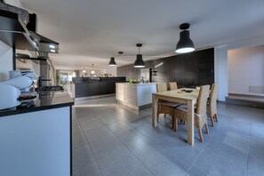 Une cuisine moderne dotée d’un îlot central, d’un éclairage suspendu et d’un coin repas avec des chaises en osier.
