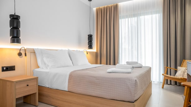 Una camera d'albergo moderna con un letto in legno, lampade ai comodini, una poltrona e un'ampia finestra con tende.