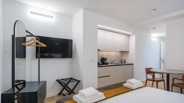 A modern hotel room with a bed, a desk, a TV, a kitchen area, and a dining table. - Hotiday Trieste Teatro (Trieste)