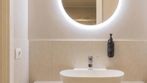 Une salle de bain avec un miroir rond, un lavabo blanc et un flacon de savon pour les mains fixé au mur.
