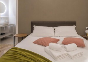 Ein Hotelzimmer mit Bett, Kissen, Nachttisch, Lampe und Spiegel.