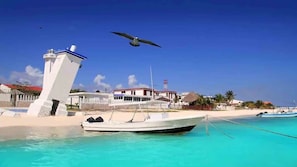 A boat docked at a beach with a lighthouse and buildings in the background. - VILLA PRINCE,loft&rooftop,pool&jaccuzi 2kitch 5brm (Puerto Morelos)