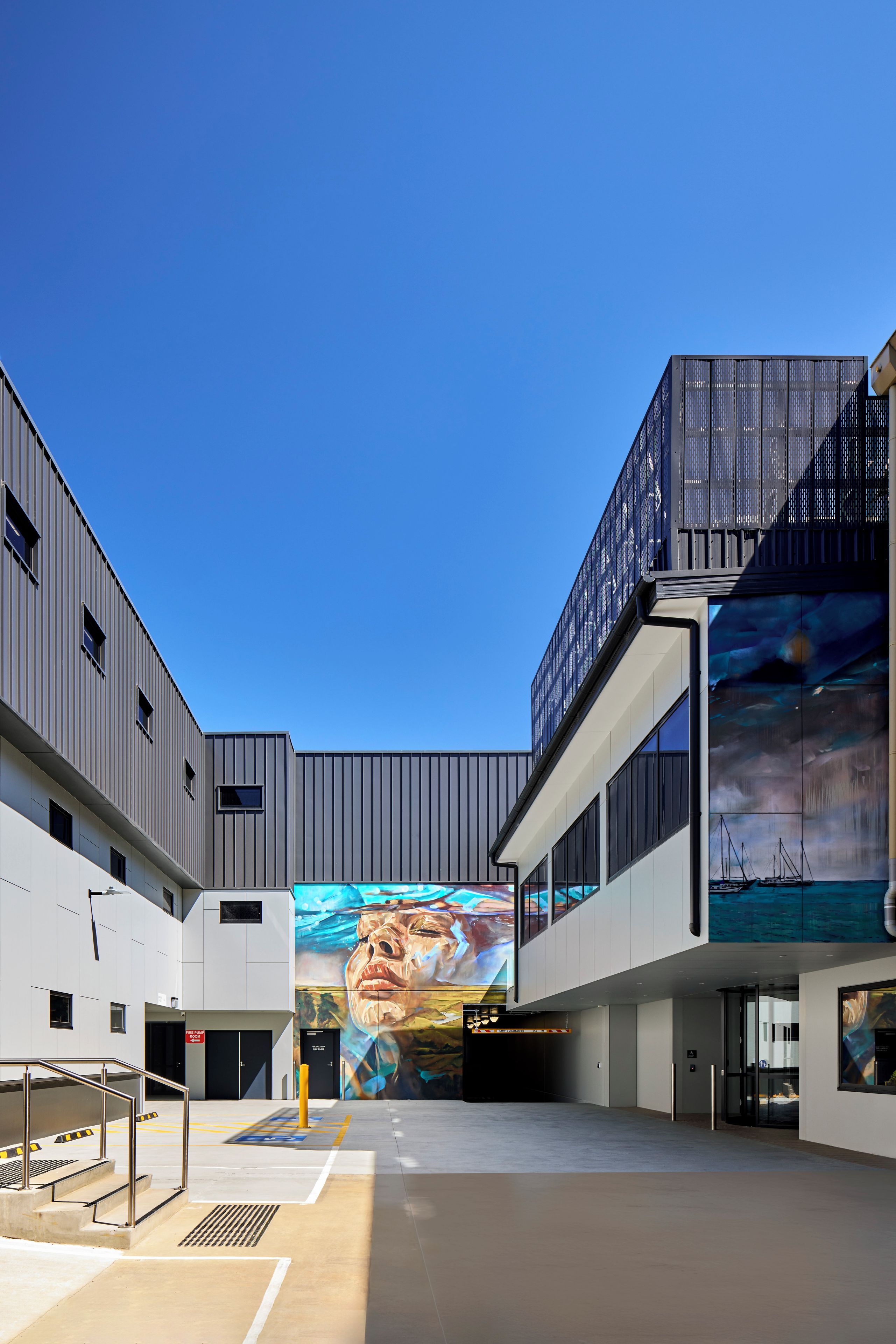 A modern building with a large mural, a staircase, and a clear blue sky.