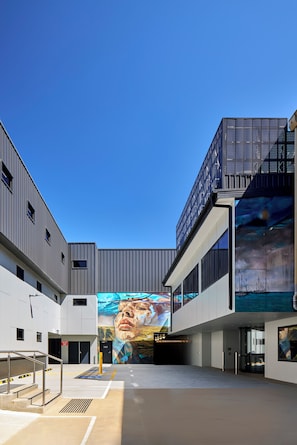 A modern building with a large mural, a staircase, and a clear blue sky. - Bayside Geelong Hotel & Apartments (Geelong)