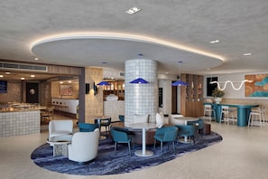 A modern hotel lobby with a central seating area, a bar, and a large mural on the wall.