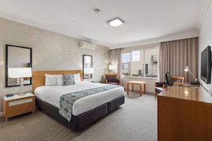 A hotel room with a large bed, a desk, a chair, a TV, and a window with curtains. - Bayside Geelong Hotel & Apartments (Geelong)