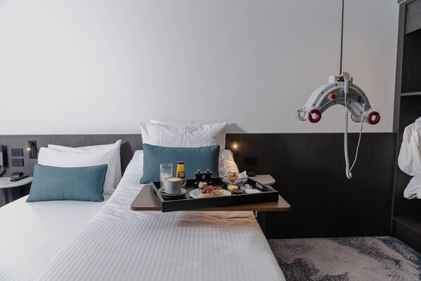 A hotel room with a bed, a tray with breakfast items, a wall-mounted phone, and a headboard with a unique design.