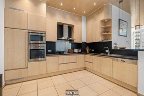 Eine moderne Küche mit Holzausstattung, einem Kombi-Backofen, integriertem Kochfeld und einer schwarzen Arbeitsplatte.