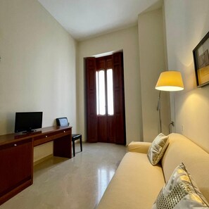 A room with a desk, a chair, a television, a sofa with cushions, a lamp, and a door. - Hotel San Sebastiã¡n Hospederã­a (Cieza)