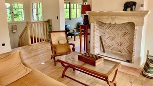 A spacious living room with a wooden floor, a fireplace with a geometric brick pattern, a chessboard, and a comfortable armchair. - A0003 Newly renovated villa with pool and bay view steps from the beach (Lège-Cap-Ferret)