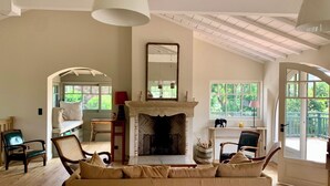 A spacious living room with a fireplace, comfortable seating, and large windows offering views of the outdoors. - A0003 Newly renovated villa with pool and bay view steps from the beach (Lège-Cap-Ferret)