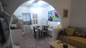 Un salon chaleureux avec un canapé, une table à manger et une cuisine visible à travers une arche.