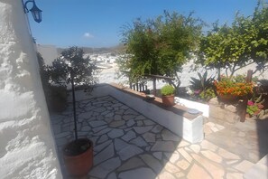 A stone-tiled patio with potted plants and a view of a white building in the background.