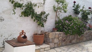 Un mur blanc orné de plantes grimpantes, un bac en pierre rempli de fleurs et deux pots en terre cuite.