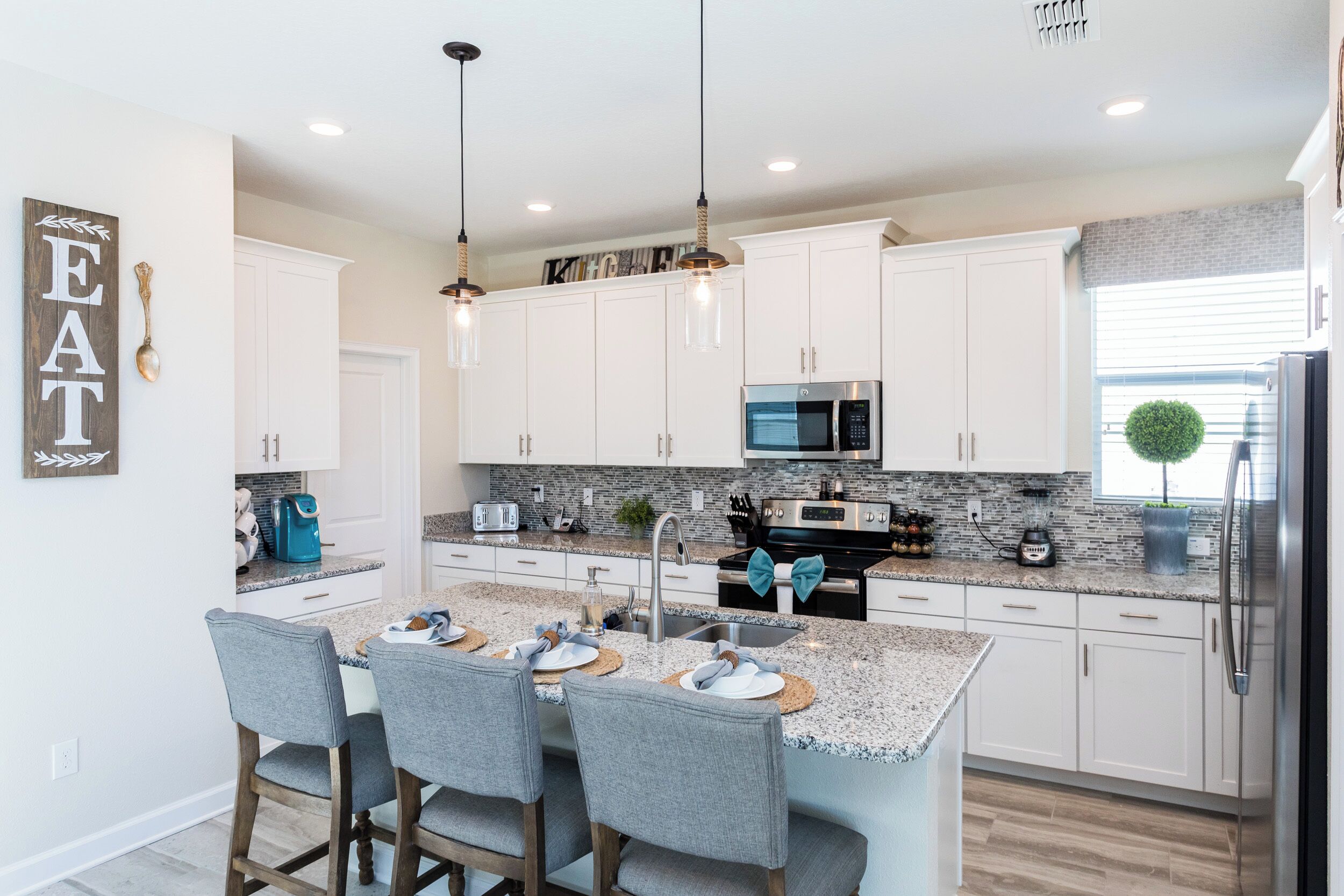 A modern kitchen with white cabinets, granite countertops, and stainless steel appliances. There is a dining area with bar stools and a large island.