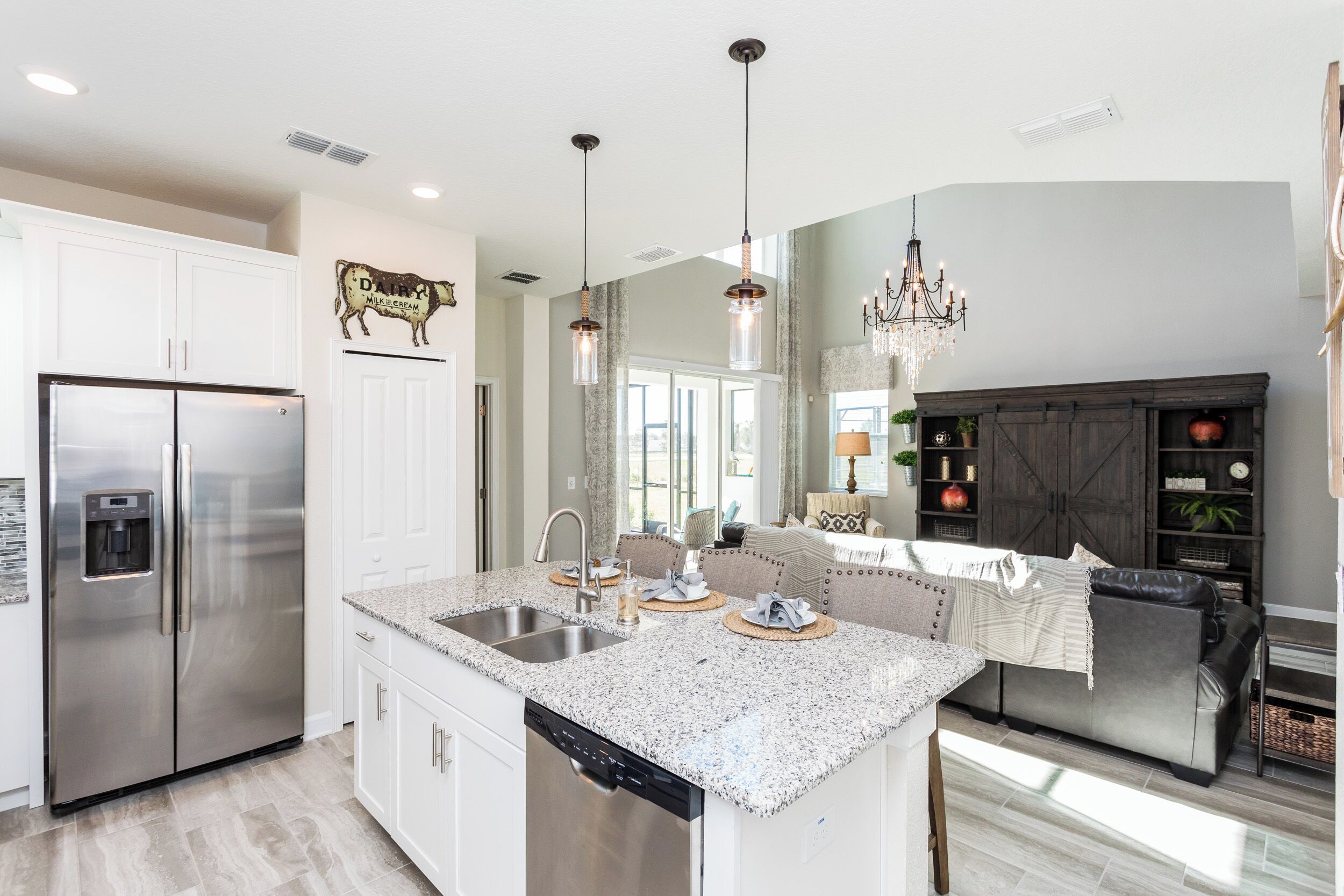A modern kitchen with a stainless steel refrigerator, a dishwasher, and a granite countertop island with a sink.