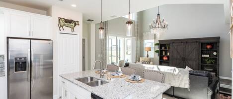 A modern kitchen with a stainless steel refrigerator, a dishwasher, and a granite countertop island with a sink.