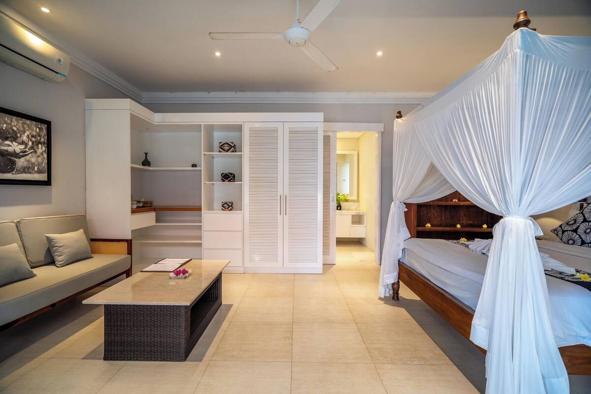 A bedroom with a canopy bed, a sofa, a coffee table, a wardrobe, and a ceiling fan.