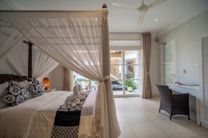 A bedroom with a canopy bed, a desk with a chair, and a view of the outside.